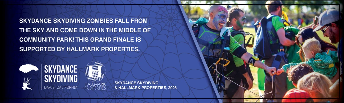 Skydivers in zombie face paint land in the park as a crowd of children watches.