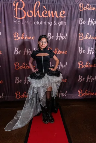 A woman in a black and white steampunk dress poses in front of the Boheme photo backdrop.