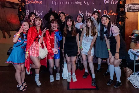A group of ten friends in zombie makeup and costumes pose together at the Boheme photo backdrop.
