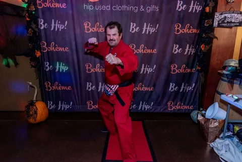 A man in a red karate gi strikes a fighting stance in front of the Boheme photo backdrop.