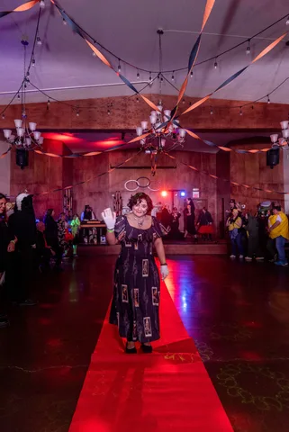A woman in a vintage patterned dress and doll-like zombie makeup waves down the red carpet.