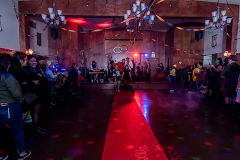 The ballroom floor and red carpet runway seen wide, crowd lining both sides under string lights.