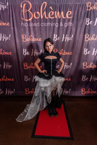 A woman in a black and white steampunk dress poses again at the Boheme photo backdrop.