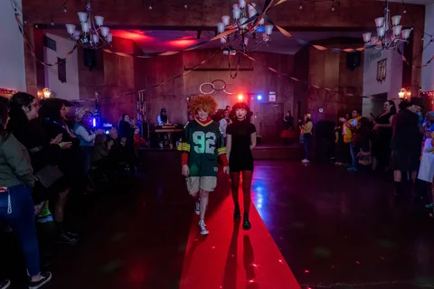 A person in a green jersey costume walks the red carpet runway.