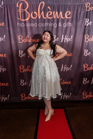 A woman in a flowing white gown poses confidently at the Boheme photo backdrop.
