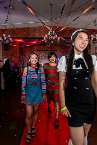Three friends dressed as horror movie characters laugh together on the red carpet.