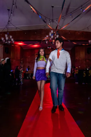 A couple in matching cartoon-mystery costumes walk arm in arm down the red carpet.