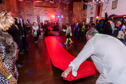 A candid moment as someone rolls out the red carpet in front of a costumed crowd.