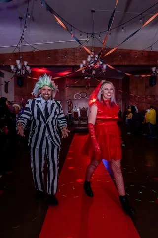 A man in a black and white striped suit and a woman in a red dress laugh walking the red carpet.