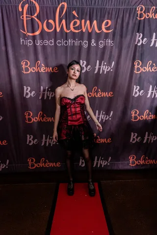 A woman in a red and black corset dress poses at the Boheme photo backdrop.