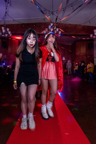 Two young women in zombie makeup and costumes laugh together on the red carpet.