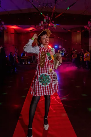 A woman in a homemade picnic basket dress grins and tips her straw hat on the red carpet.