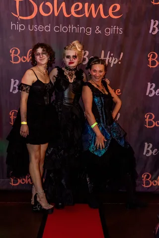 Three women in elaborate gothic gowns and dramatic makeup pose at the Boheme backdrop.
