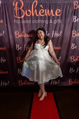 A woman twirls her white gown while laughing at the Boheme photo backdrop.
