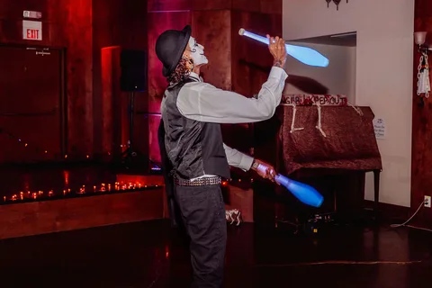 A performer juggles glow sticks with arms raised on the small stage.