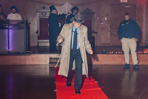 The man in the trench coat continues walking the runway, farther from camera.