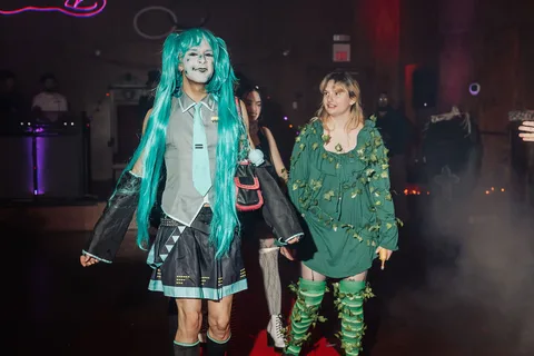 Two women in green ivy costumes walk along the red carpet runway.
