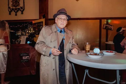 A man in a trench coat and hat walks candidly through the venue.
