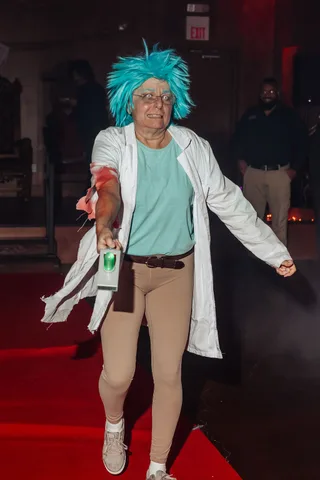 The same mad scientist costumed woman reaches out with a prop bottle.