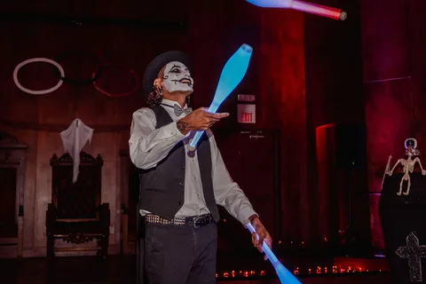 A performer juggles glowing sticks mid-motion under colorful stage lighting.