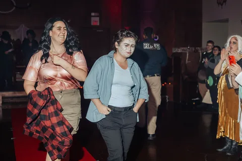 Two women walk together smiling along the red carpet runway.