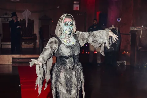A woman in a gray zombie witch costume reaches outward dramatically on the runway.