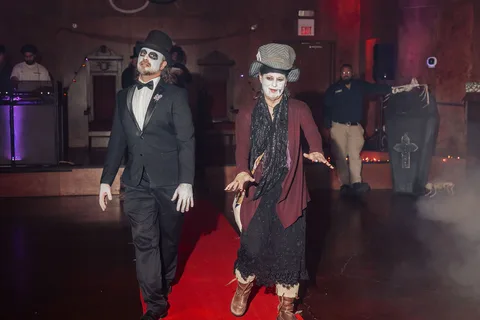 Two vampire-costumed guests walk together on the red carpet runway.