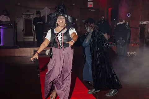 Two costumed women walk the runway with a hand raised.