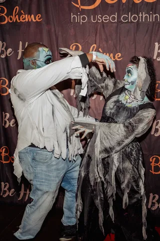 Two guests in gray zombie makeup act out a dramatic moment, one reaching toward the other's face.