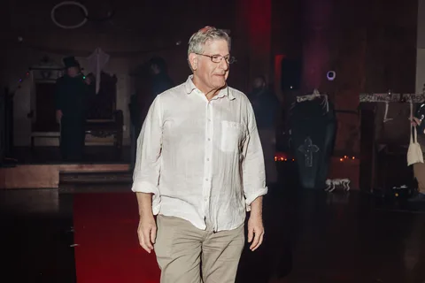 A man in a white shirt walks alone through the dim venue.