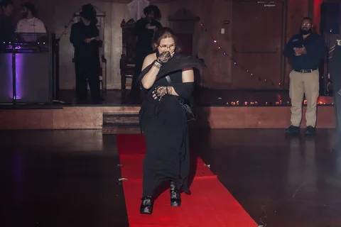 The same masked figure continues walking the runway.
