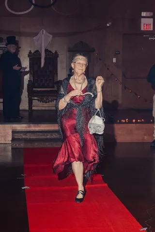The same woman in a red dress continues down the runway, farther from camera.