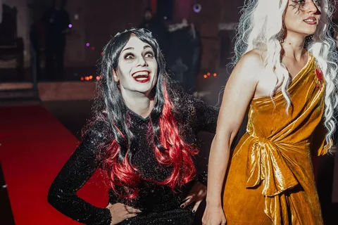 Two women in black sequin and gold gowns laugh joyfully together on the runway.