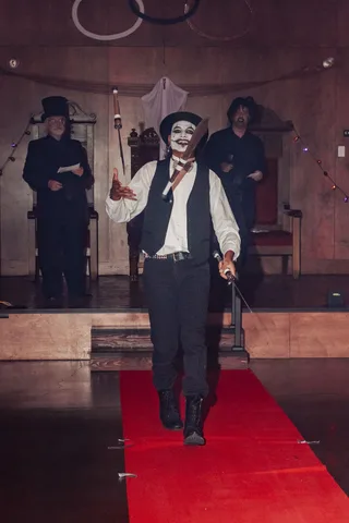 Two men in top hats perform with a raised cane on the runway.