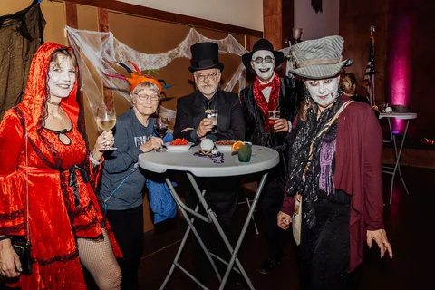 A group in top hats and red dresses gathers around a small table in costume.