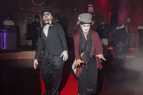 Two guests in gothic vampire costumes and pale makeup pose dramatically on the runway.