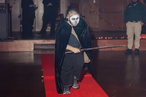 A figure in a black robe and skull mask walks the runway.