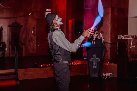 A performer in white face paint juggles glow sticks mid-toss.