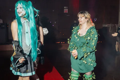 Two women in costume stand together on the red carpet runway.