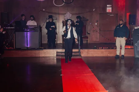 A man in costume walks the runway, seen at a distance in low light.