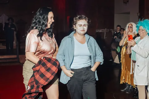 Two women laugh together while walking the red carpet runway.