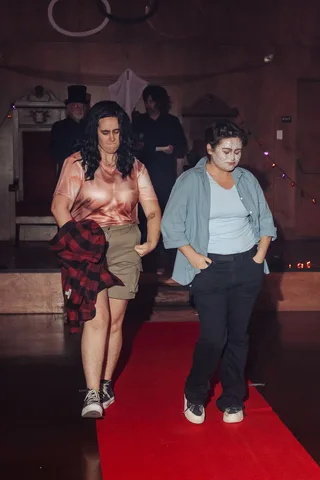 Two women walk further along the red carpet runway.