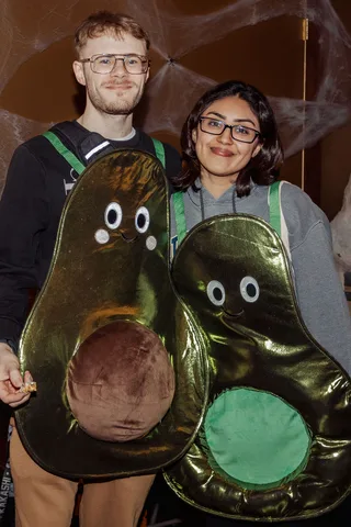 A couple in matching avocado costumes pose smiling for the camera.