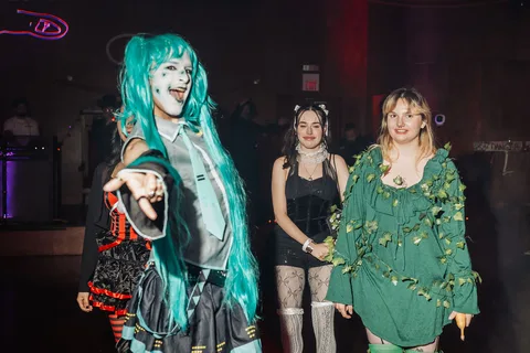 A woman in a teal wig points playfully at the camera on the red carpet runway.