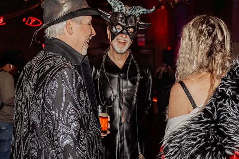 A man with horned headwear laughs with two other guests in costume.