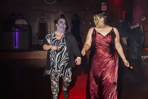 The same two women in gowns continue walking together down the runway.