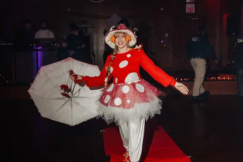 A woman in a mushroom costume twirls her umbrella mid-motion on the runway.