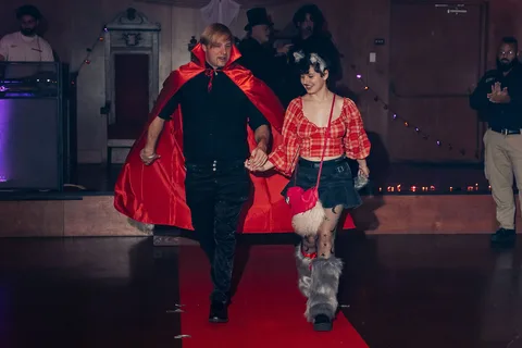 A couple in costume walk hand in hand along the red carpet runway.