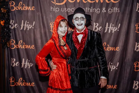 A couple in a striking red robe and black tuxedo pose dramatically in front of the Boheme backdrop.