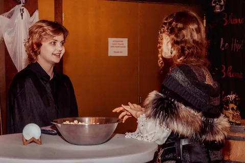 Two women in witch costumes stand at a fortune-telling table with a lit crystal ball.